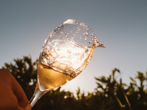 Glass of golden wine splashes in hand against the sunset sky. The sunlight enhances the sparkling bubbles, creating a refreshing and dynamic scene