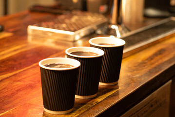 Three steaming takeaway cups of hot chocolate on a rustic wooden counter, lit by warm ambient...