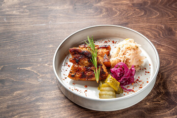 A beautifully arranged plate featuring grilled pork with crispy skin, accompanied by pickles, purple cabbage, and fresh herbs. The dish showcases vibrant colors and textures