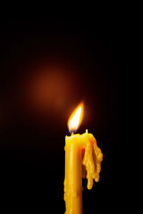 Yellow candle melting with flame on black background