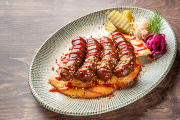 A vibrant plate featuring grilled sausages drizzled with sauce, served on a bed of flatbread. Accompanied by pickles and colorful cabbage, it offers an enticing presentation.