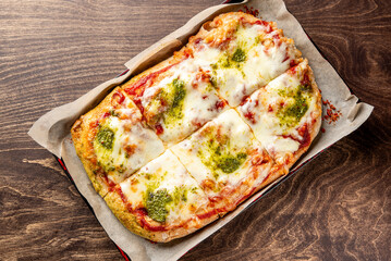 A freshly baked rectangular pizza topped with melty cheese and vibrant green pesto. The golden crust is perfectly crisp, making it an inviting and delicious meal option.
