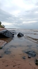 Fototapeta premium Serene Coastal Scene Dark Rocks Sandy Beach Calm Ocean Waves Cloudy Sky
