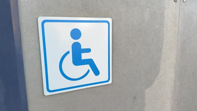 Close up of blue wheelchair accessibility sign on wall, minimal urban element representing inclusive access and emergency assistance for disabled individuals