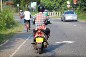 A man on a motorcycle is riding down a road with a car behind him