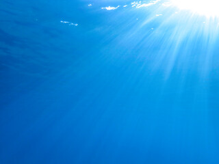 Dark blue ocean surface seen from underwater. Abstract waves underwater and rays of sunlight shining through, Sun light rays undersea deep, Underwater background with sea bottom, Mediterranean sea.