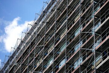 Fototapeta premium Building facade undergoing renovation with scaffolding against a blue sky background. The intricate structure of the scaffolding and the building's architecture create a dynamic contrast.