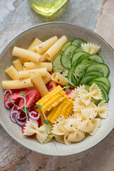 Pasta salad with farfalle, tortiglioni and vegetables, vertical shot on a grey and roseate granite surface, closeup