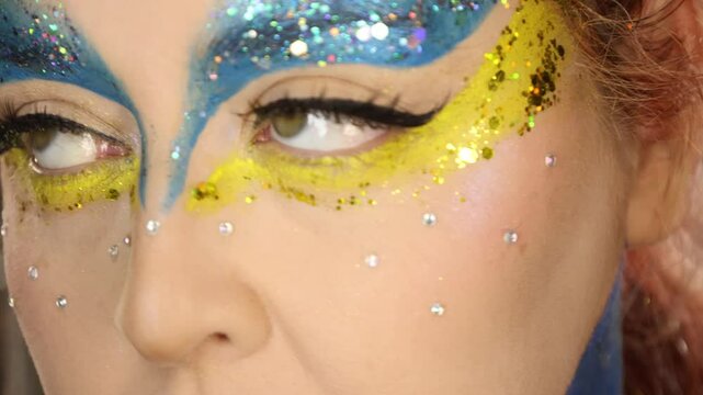 Tropical carnival-inspired makeup with bold blue and yellow tones, glitter, and leaf accessories &mdash; a tribute to the blue macaw from Rio in a Cirque du Soleil fantasy style.