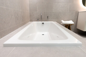 Modern built-in ceramic bathtub with stainless steel and chrome faucets in a contemporary bathroom...