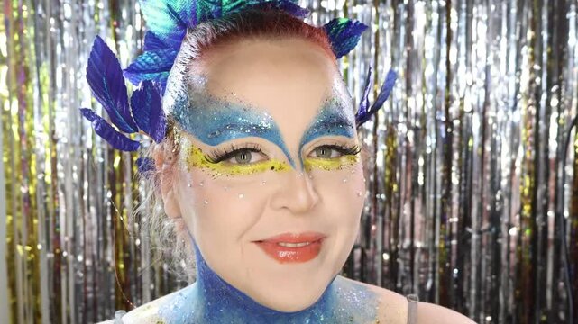 Tropical carnival-inspired makeup with bold blue and yellow tones, glitter, and leaf accessories &mdash; a tribute to the blue macaw from Rio in a Cirque du Soleil fantasy style.