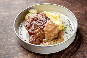 A hearty plate featuring a juicy meatloaf topped with rich brown gravy, served alongside creamy mashed potatoes and pickles. The presentation is inviting and comforting