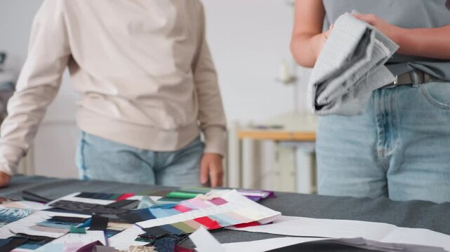 Garment maker unfolding elastic material on table filled with colorful fabric samples and sewing patterns, preparing textiles for tailoring project in creative workspace with tools