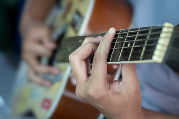 A young man is playing yellow and brown guitar in a rather dark room with lighting from the lights, during the day