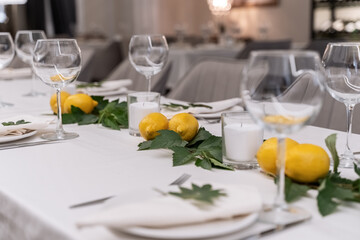 beautiful table decoration in restaurant. festive table setting in restaurant. white tablecloth on table, wine glasses, white plates, lemons, candles are burning. romantic atmosphere