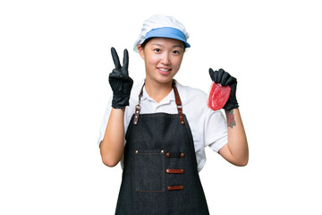 Young caucasian woman wearing an apron and serving fresh cut meat over isolated background smiling and showing victory sign
