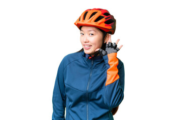 Young cyclist woman over isolated chroma key background listening to something by putting hand on the ear