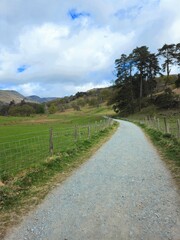 A rural gravel path in Rydal, Lake District lined with wire fencing, heading into scenic hills and open countryside. Ideal for walking, travel, and outdoor themes.