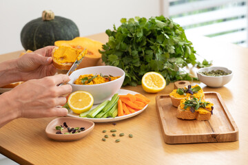 Female preparing healthy vegan pumpkin spread with fresh vegetables and herbs. Pumpkin hummus