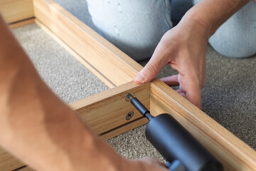 Close-up of a man assembling furniture with a cordless drill. DIY furniture assembly. Instructions