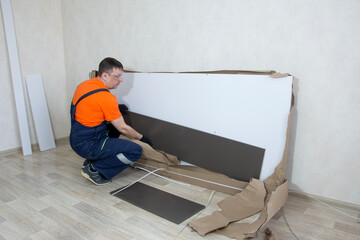 A man in overalls collects furniture from a package in close-up in a bright room