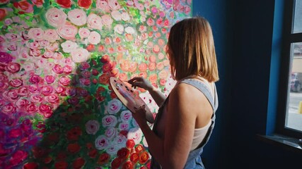 Talented artist delicately adds paint to a large canvas covered in roses, her shadow cast upon the artwork as natural light streams through the window in art studio - Powered by Adobe