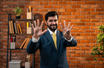 Corporate Indian man counting digits with fingers while standing in office against brick wall