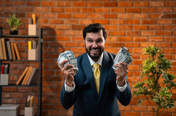 Smiling Indian entrepreneur proudly holding wad of INR notes inside brick-walled workspace