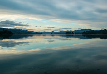 Fototapeta premium Serene Lake Reflection at Dawn: Calm Water, Misty Sky