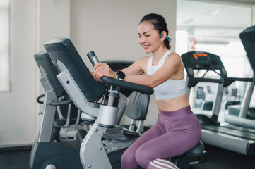 Fototapeta premium Empowered Woman Crushing Her Exercise Goals Smiling In Gym On An Exercise Bike, Toned Physique While Wearing White Sports Bra, Focused Workout With Fitness Equipment Smartwatch, Boosting Weight Loss