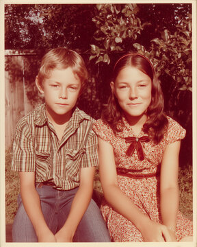 brother and sister vintage faded old photo with scratches sitting outside in backyard 1970s
