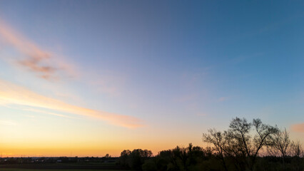 Obraz premium A tranquil sunset view over a rural landscape, showcasing vibrant colors in the sky at dusk, with silhouettes of trees framing the scene, ideal for nature-inspired themes.