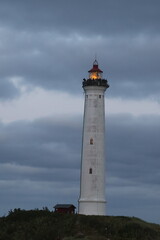 Farol &agrave; beira-mar com um c&eacute;u nubaldo e o sol a p&ocirc;r-se