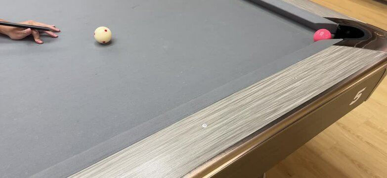 Hand preparing to shoot with a cue stick on a gray pool table, aiming at the cue ball with several balls scattered around. Focus on precision, strategy, and billiard gameplay.