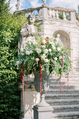 Obraz premium Bouquet of flowers stands in a stone vase near a statue in a green garden