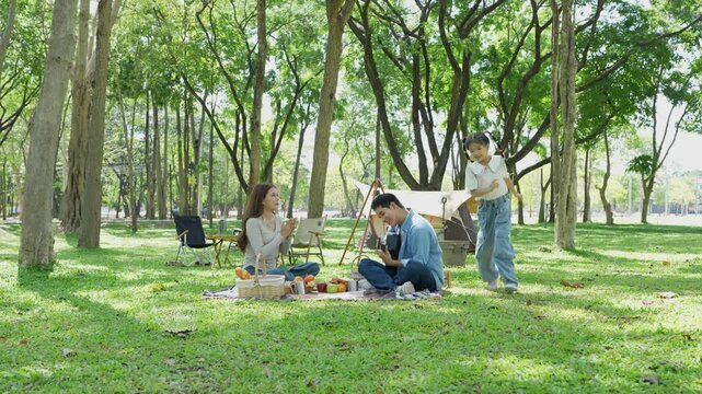 Happy Asian family camping in a park enjoying the outdoors, celebrating a holiday party, eating dinner, playing guitar and singing together.
