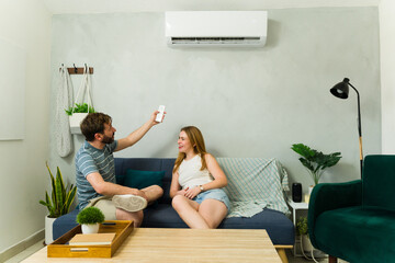 Couple relaxing on sofa using remote control for air conditioner