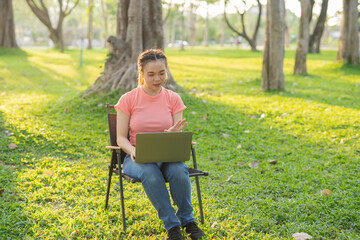Asian woman sitting working under a tree outdoors in the evening light.