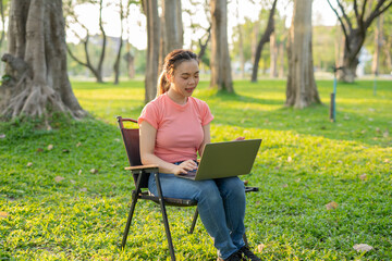 Asian woman sitting working under a tree outdoors in the evening light.