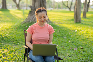 Asian woman sitting working under a tree outdoors in the evening light.
