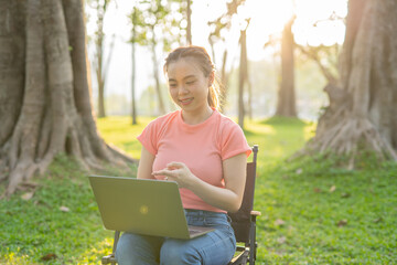 Asian woman sitting working under a tree outdoors in the evening light.