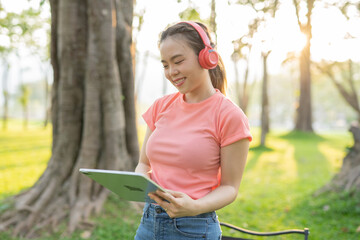 Asian woman sitting listening to music, reading a book, outdoors in nature, evening.