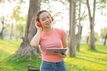 Asian woman sitting listening to music, reading a book, outdoors in nature, evening.