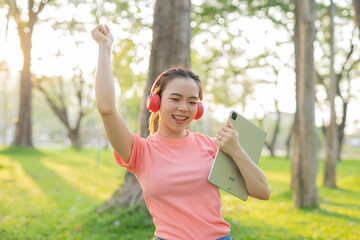 Asian woman sitting listening to music, reading a book, outdoors in nature, evening.