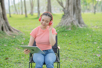 Asian woman sitting listening to music, reading a book, outdoors in nature, evening.