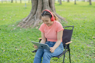 Asian woman sitting listening to music, reading a book, outdoors in nature, evening.