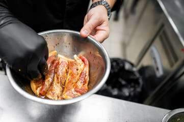 A chef in black gloves mixes marinated meat in a stainless steel bowl. The kitchen setting reflects...