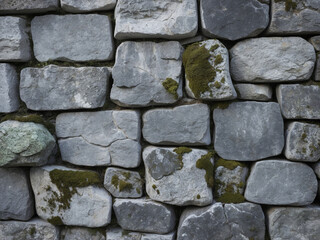 Fototapeta premium Old gray stone wall with patches of green moss growing between the irregularly shaped blocks.