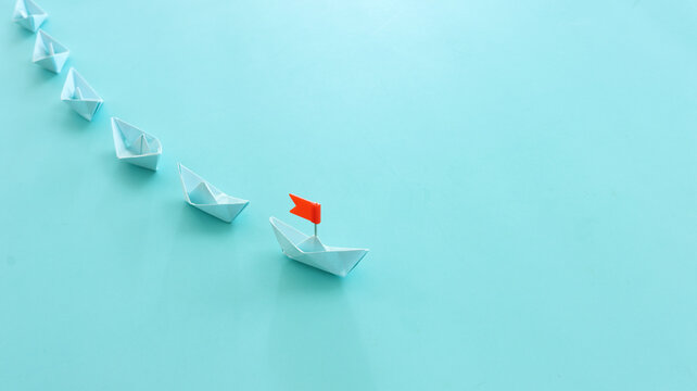 Paper boats following ahead of the leader with red flag