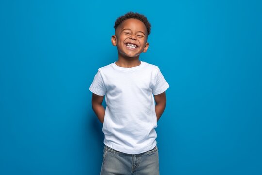 Happy smilling boy wearing bella canvas white shirt mockup, at blue background. Design tshirt template, print presentation mock-up